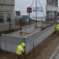 Crane lowering preformed concrete planter into the ground.