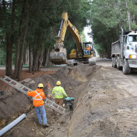 Excavator moving dirt while crew assists